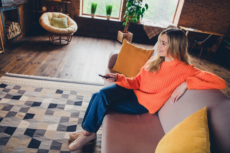 young woman sitting on sofa and holding remote while watching TV