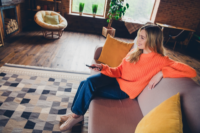 young woman sitting on sofa and holding remote while watching TV