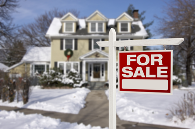 house covered in snow with For Sale sign out front
