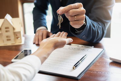 agent handing keys to buyer with signed contract on the table between them