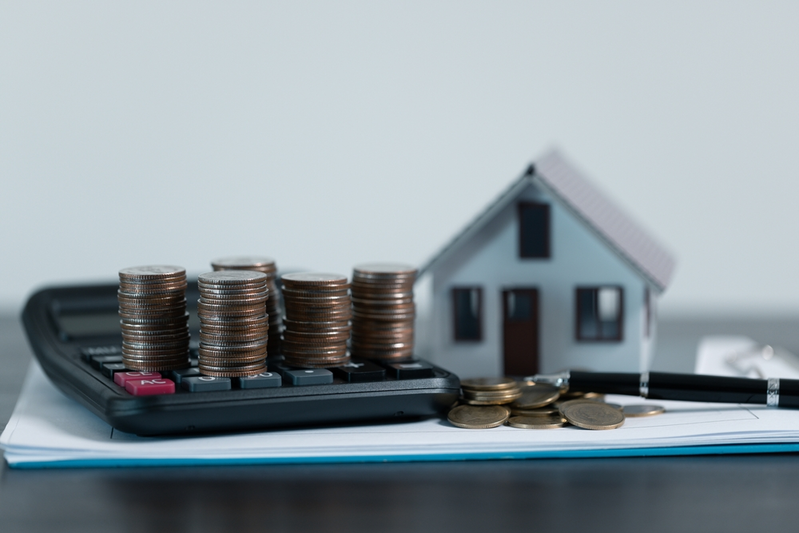 model of house next to calculator with stacks of coins
