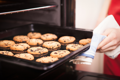 close up of hand removing pan of chocolate chip cookies from oven