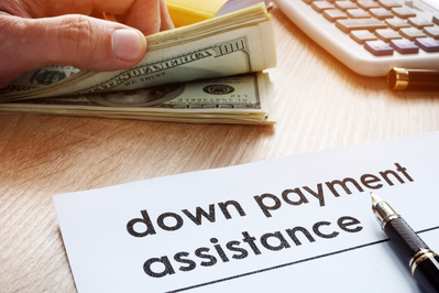 document labeled "down payment asssitance" next to stack of cash and calculator