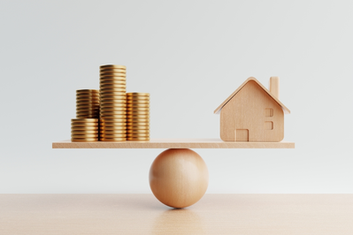 wooden model of house balanced across from stack of gold coins