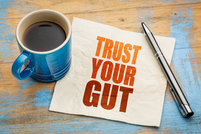 coffee mug and pen next to paper that says "Trust Your Gut"