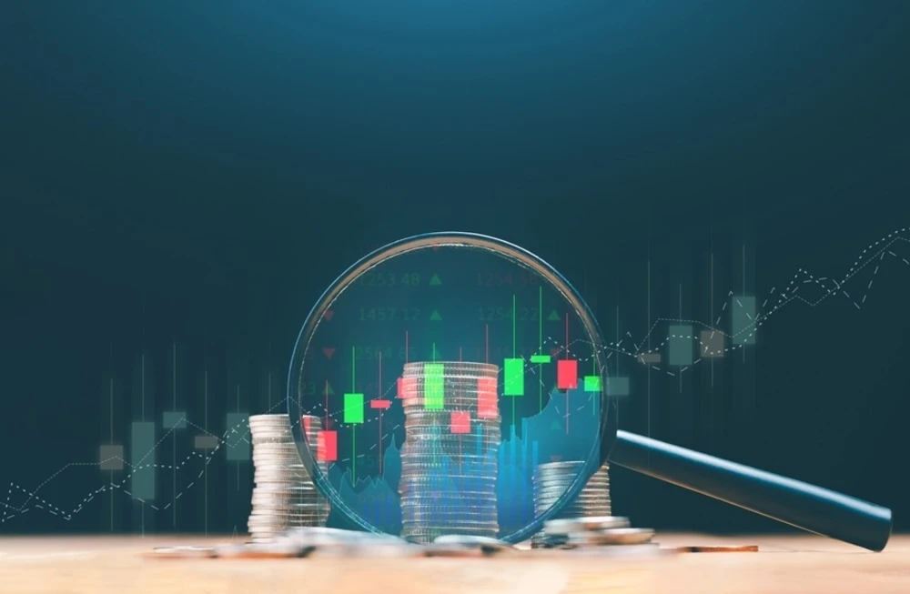 magnifying glass over stacks of coins with trend graph